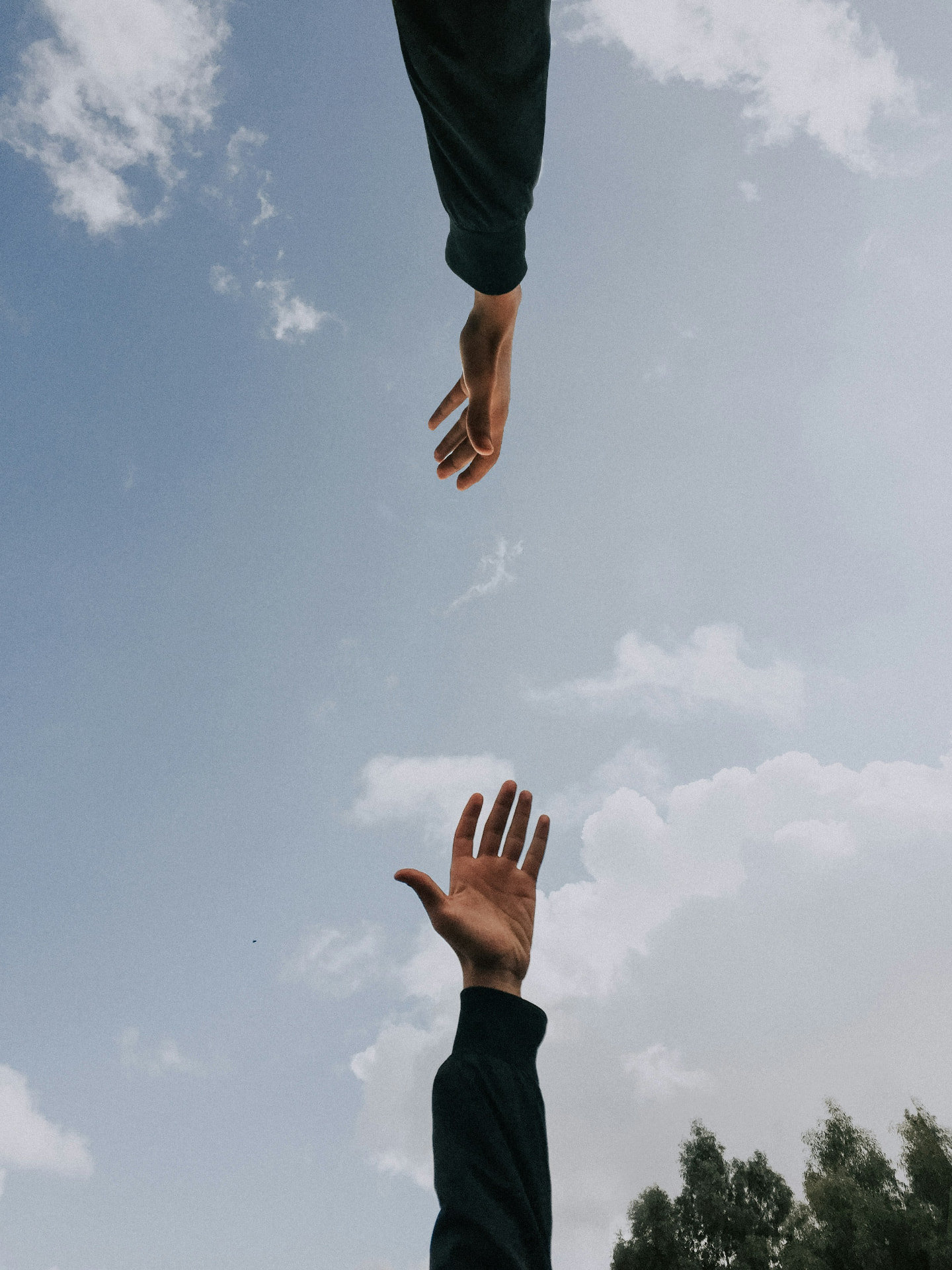 One hand reaching down toward another reaching up against an open sky