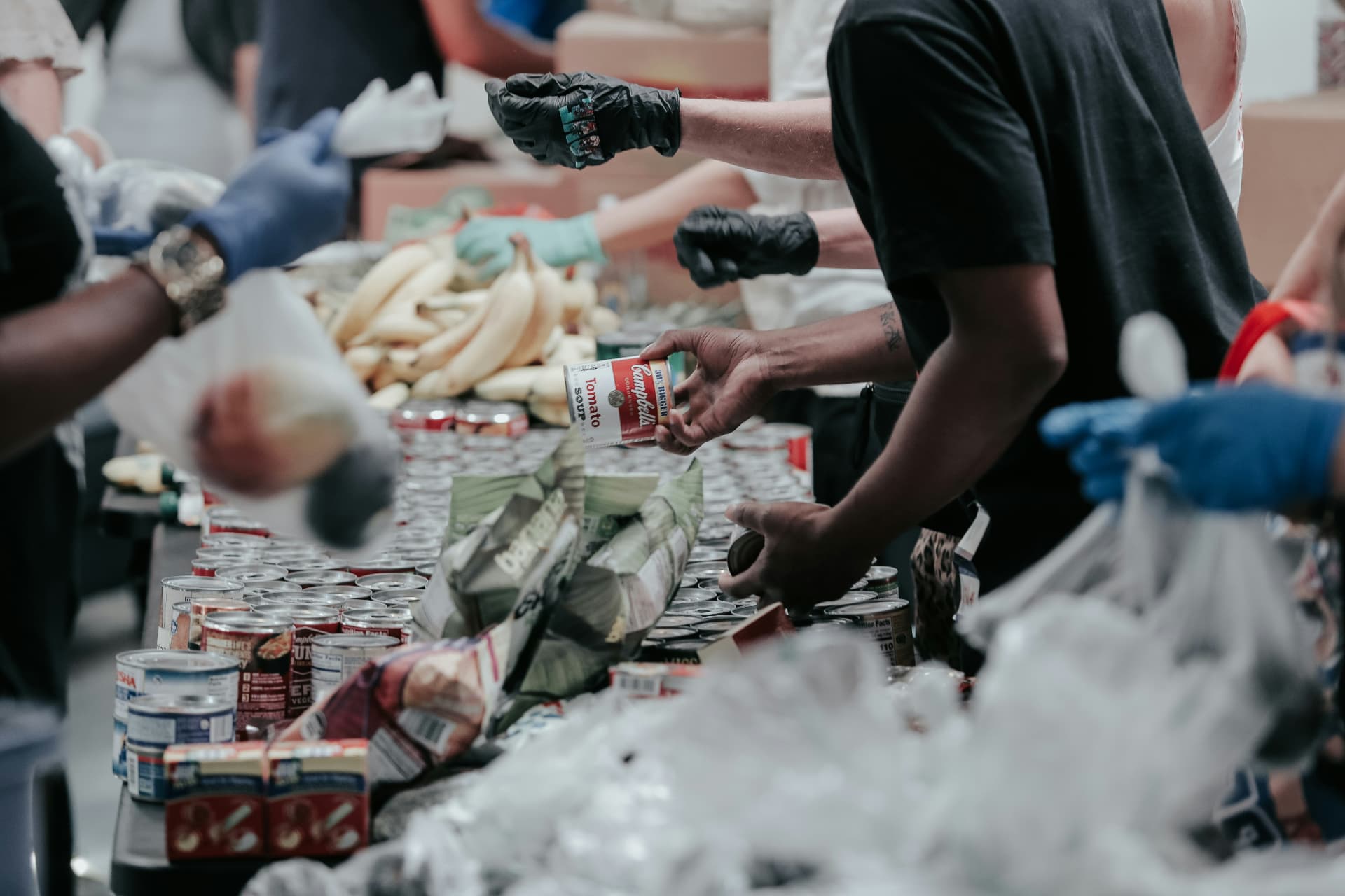 Volunteers in gloves sorting canned goods and fresh produce at a food distribution