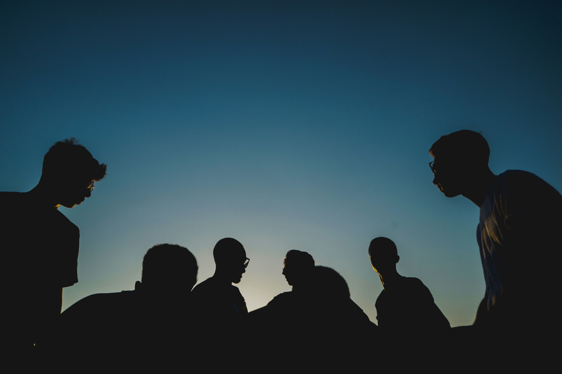 Silhouettes of people gathered in conversation against a blue dusk sky